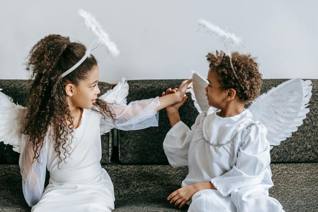 Two children dressed as angels having fun indoors, embodying joy and imagination.